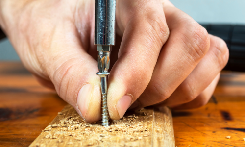 Fingers hold a screw while drilling it into a piece of wood