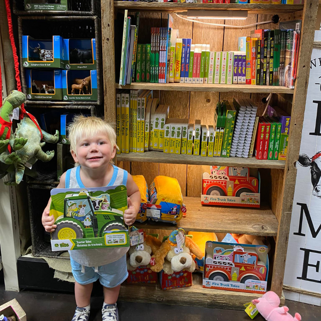 Child standing in front of Carmine's book and puzzle section holding a book